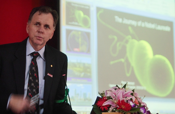 2005 年诺贝尔生理学或医学奖得主巴里·马歇尔日前在中国发表演讲，背后大屏幕上的图像即为幽门螺杆菌。（图片：China Photos/Getty Images）
